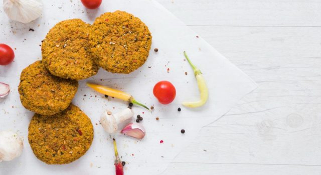Burger vegetariani su sfondo chiaro con spezie e verdure estive. Ricetta antispreco estiva con legumi, dalla cucina ciociara.