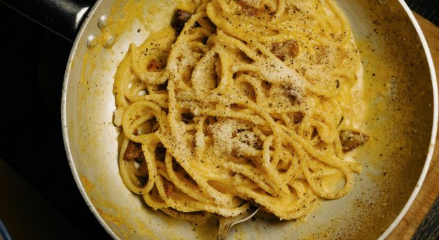 Un piatto di spaghetti alla carbonara fumanti con guanciale croccante e pepe nero